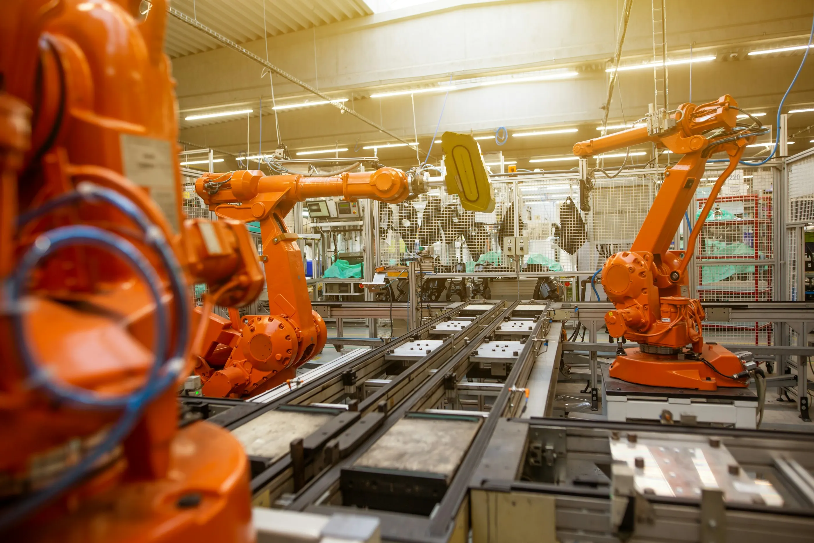 Orangefarbene Industrieroboter an einer Fertigungslinie mit Werkstückträgern und Schutzgittern