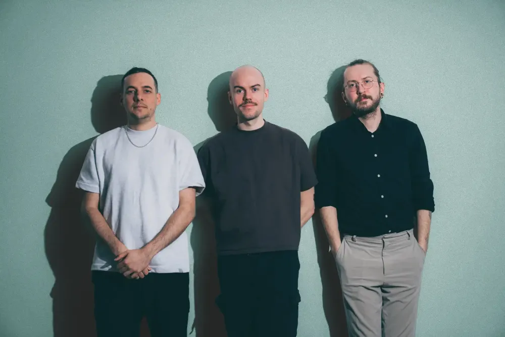 Drei Personen aus dem 022-Team vor einer grünen Wand im Studio