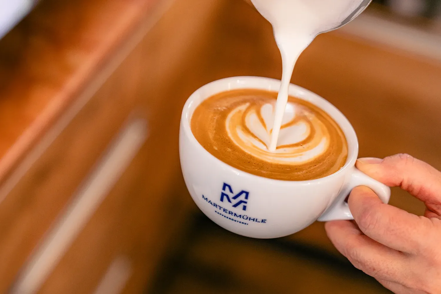 Milchschaum wird in einen Cappuccino in einer Tasse der Martermühle gegossen